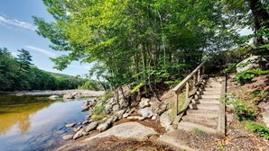 A wooden staircase leading down to a riverbank, surrounded by trees and rocks.