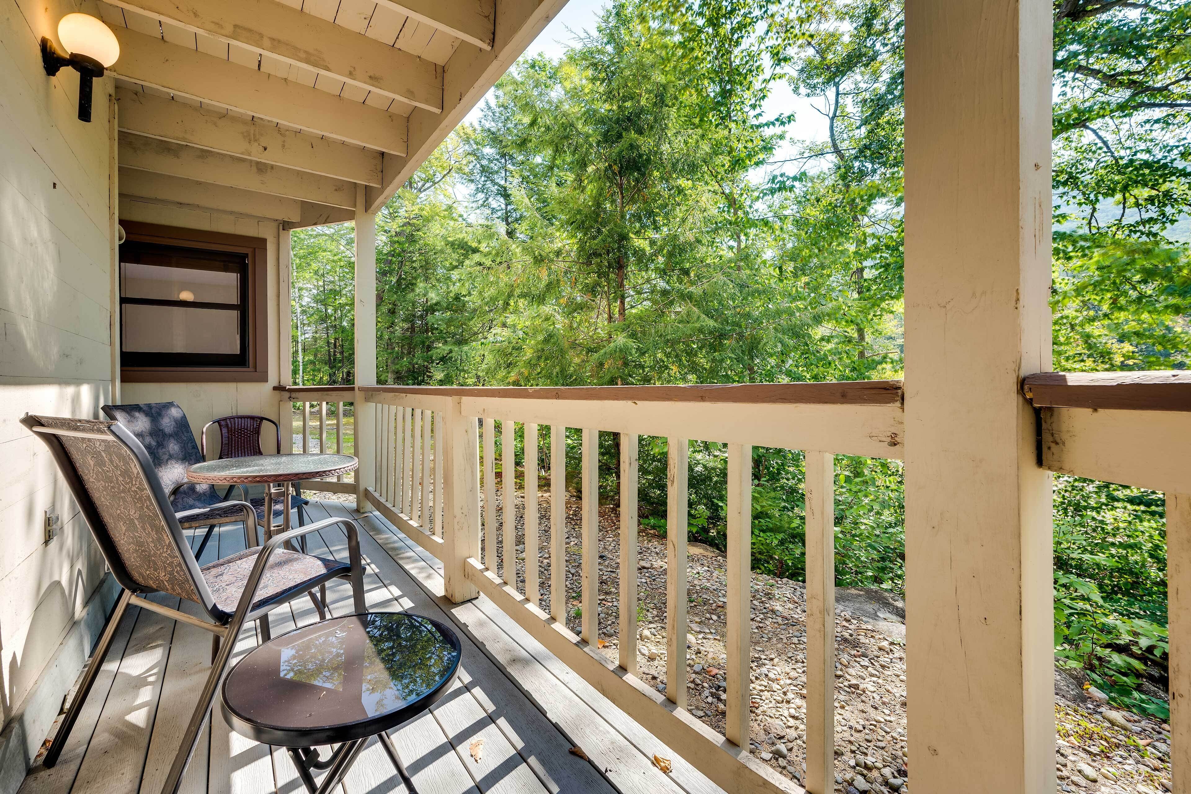 A wooden deck with outdoor seating, a window, and a view of trees.