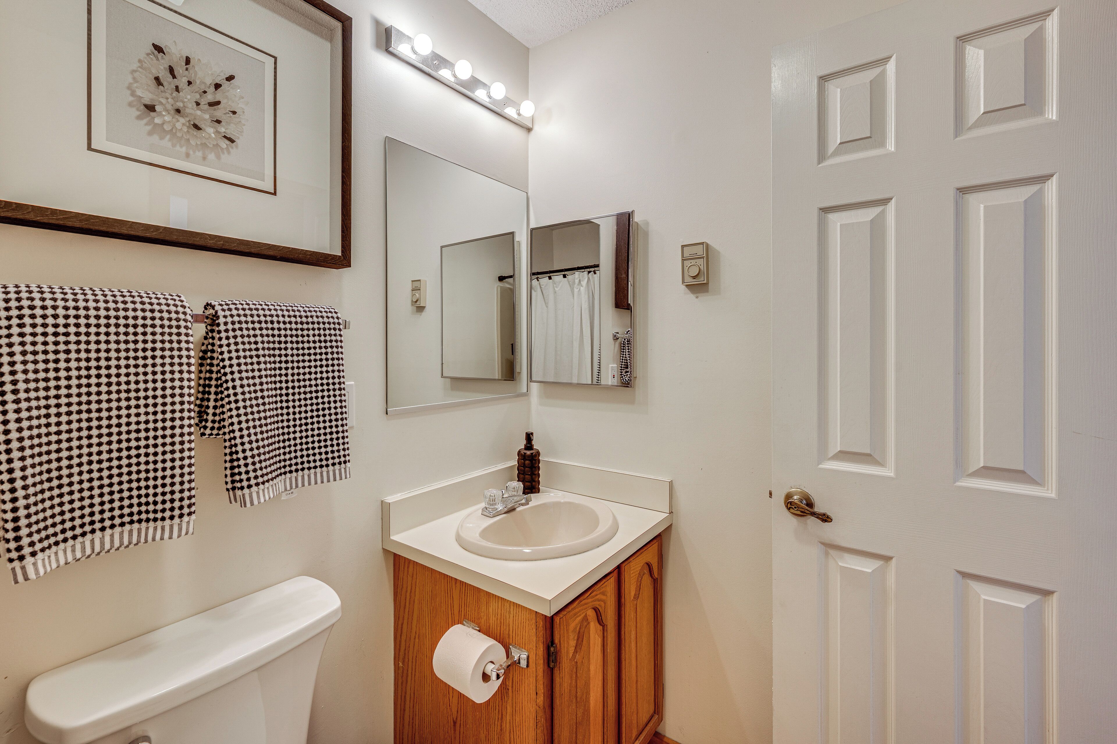 A bathroom with a toilet, sink, and mirror. There are towels hanging on the wall and a framed picture above the mirror.