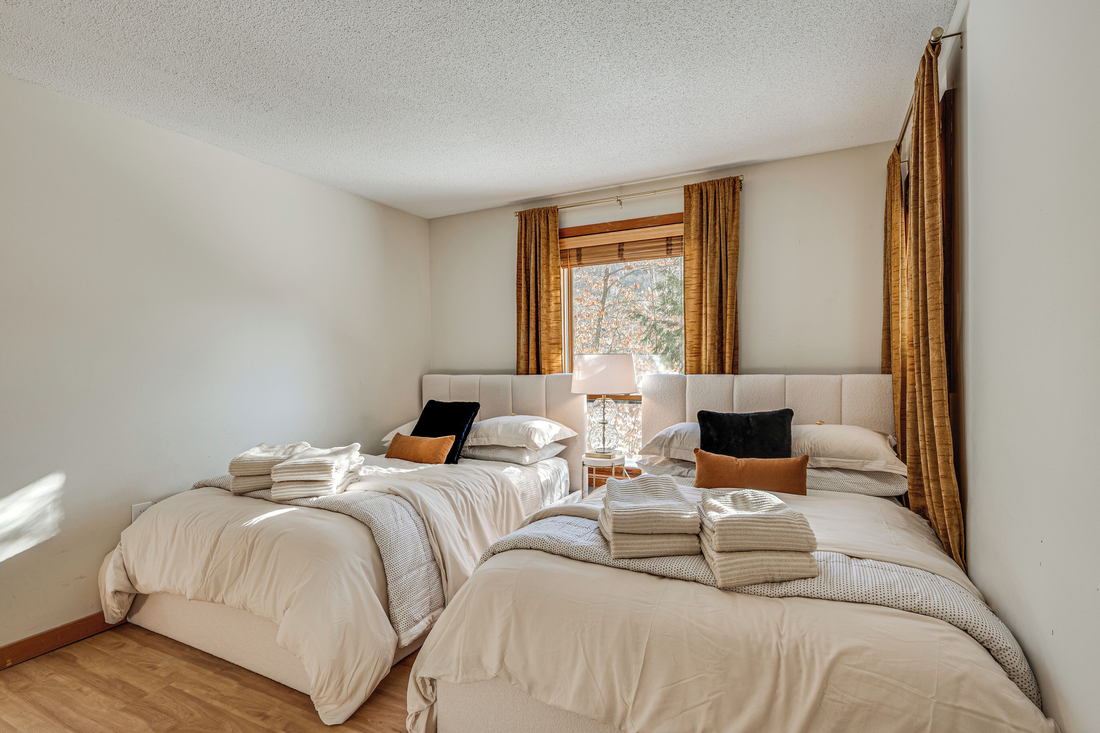 A bedroom with two beds, a nightstand, a lamp, and a window with curtains.