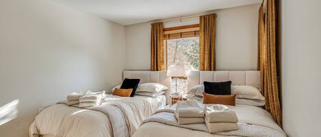 A bedroom with two beds, a nightstand, a lamp, and a window with curtains.