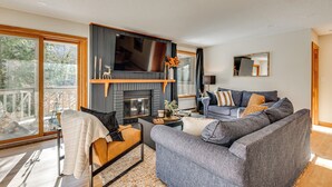 A modern living room with a fireplace, grey sofa, and a large window overlooking a deck.