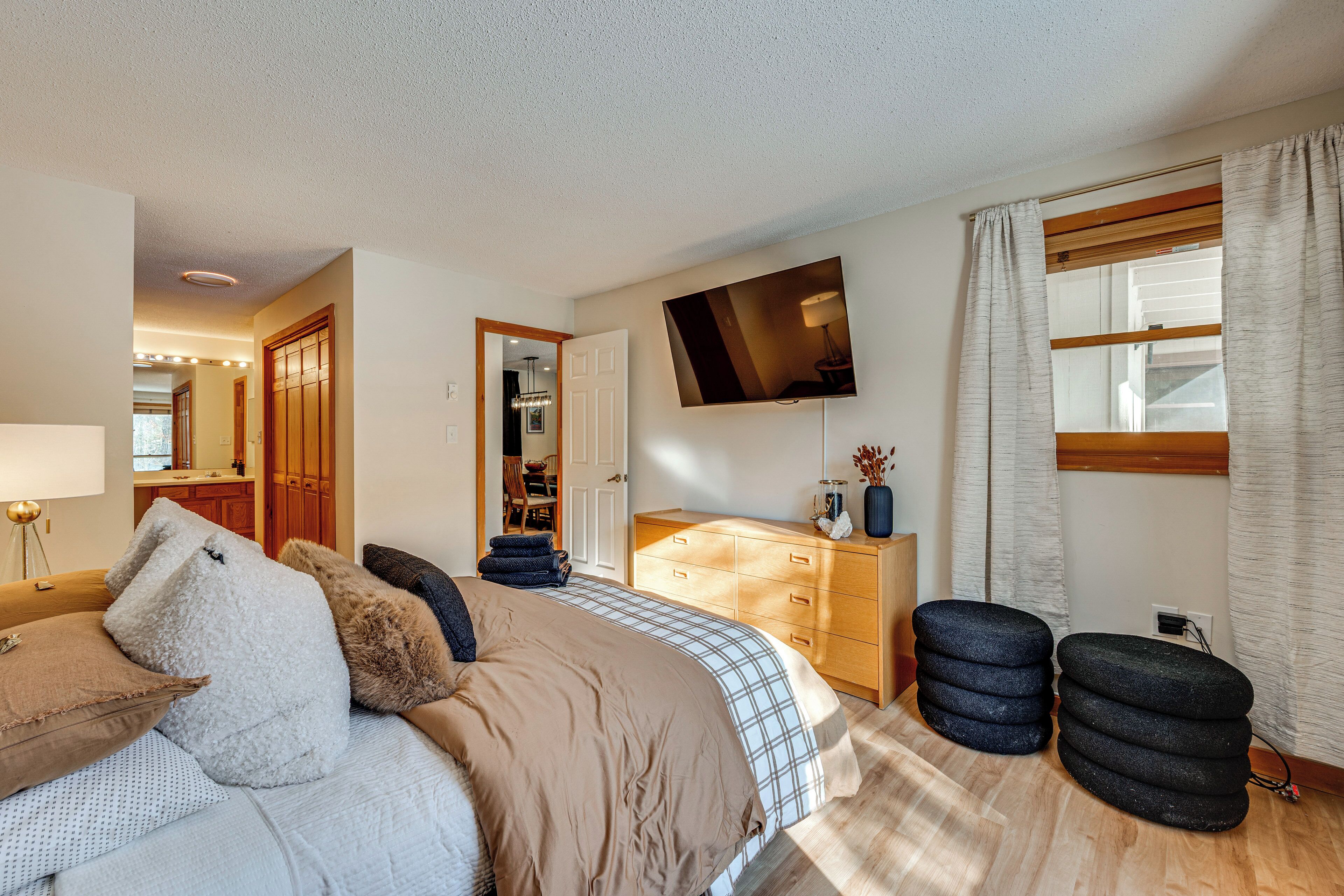 A bedroom with a bed, a dresser, a TV mounted on the wall, and a window with curtains.