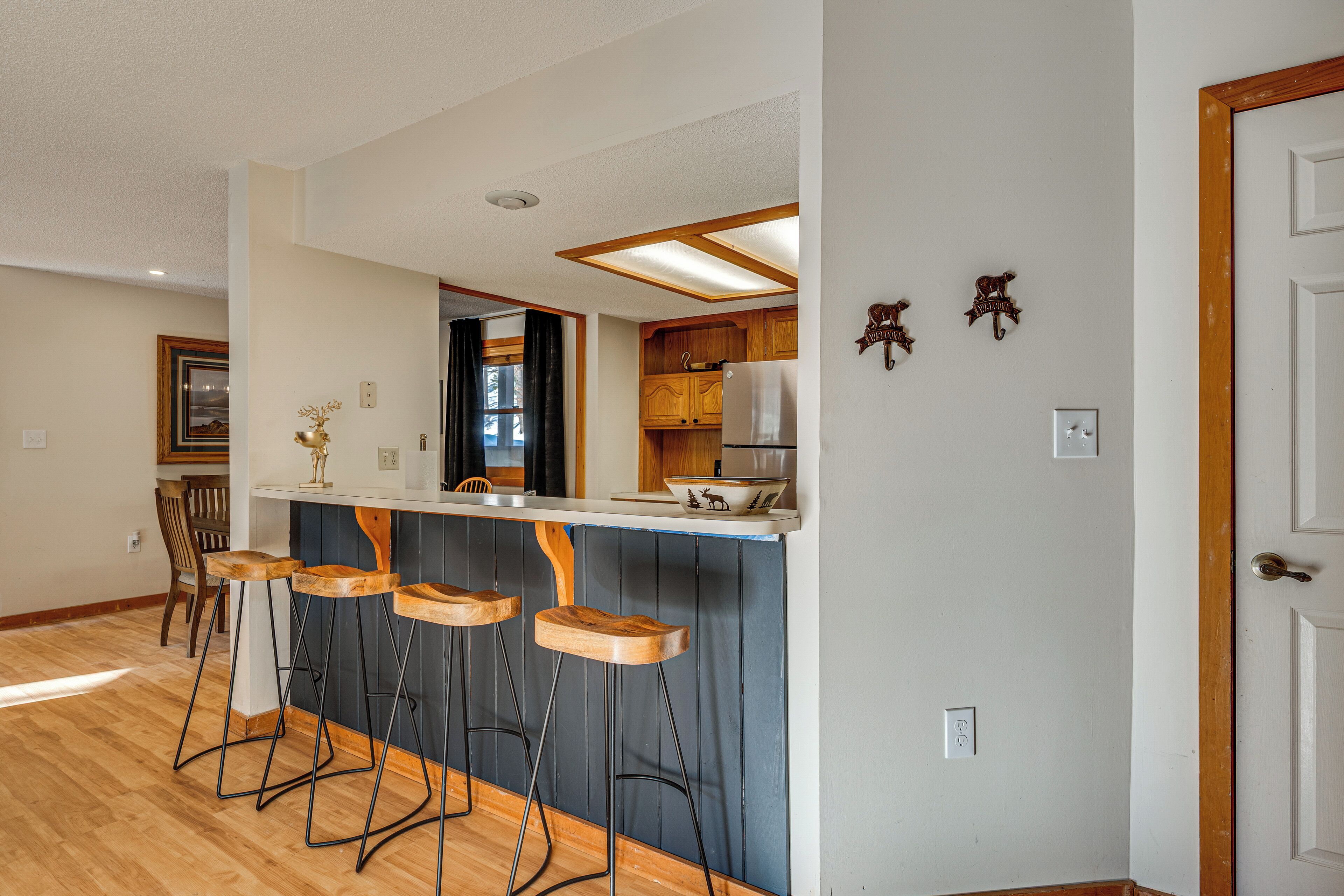 A kitchen with wooden bar stools, a refrigerator, and a window with curtains.