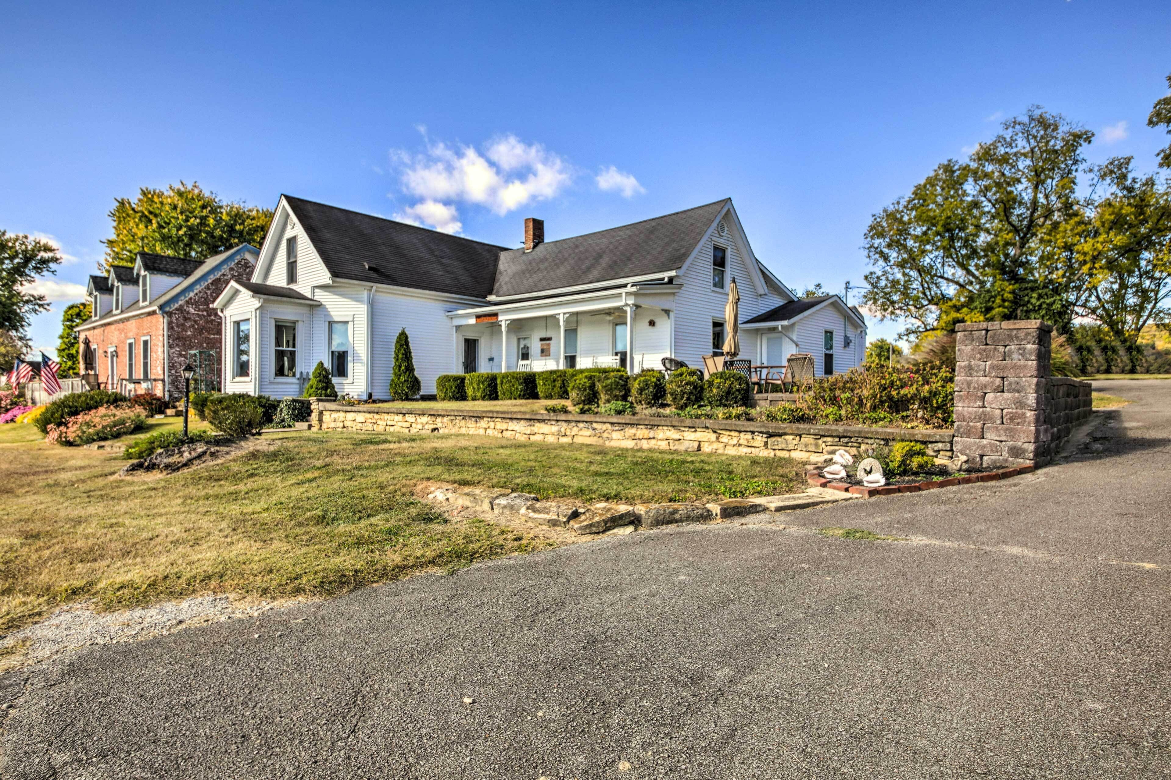 A large white house with a dark roof, a stone wall, and a well-maintained lawn.
