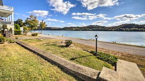 A lakeside property with a grassy lawn, a paved walkway, and a building with a balcony overlooking the water. - 1872 Bethlehem Home w/ View of Ohio River! (Otto)