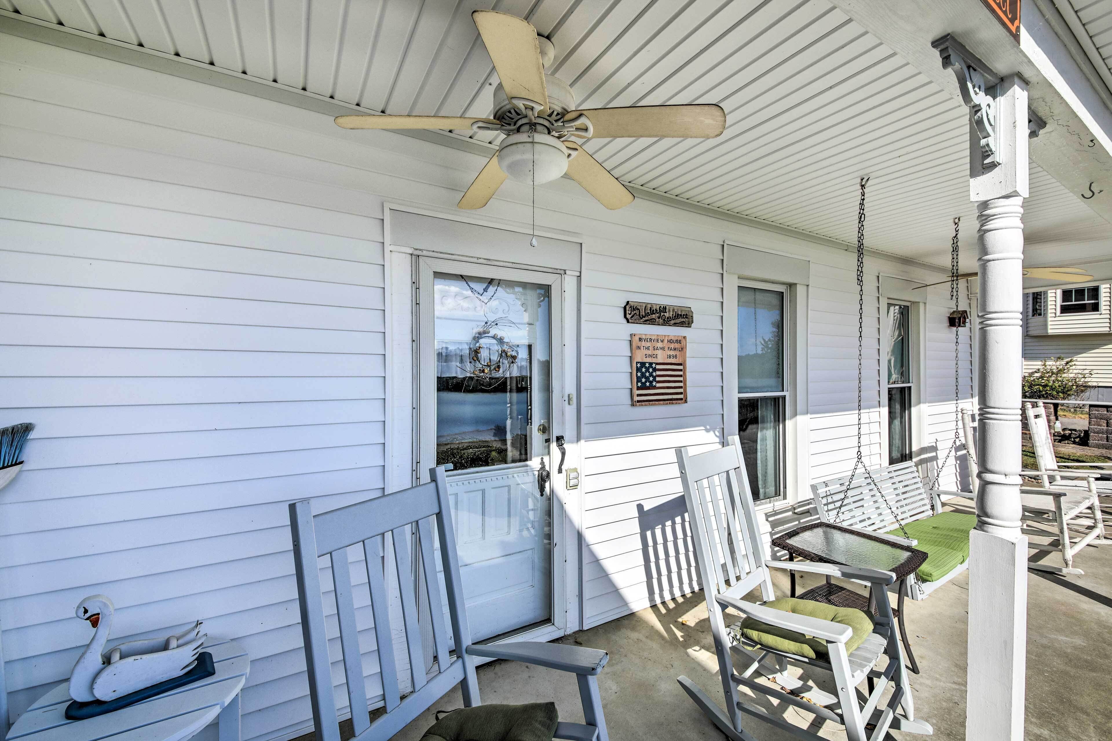 A porch with white wooden railings, a ceiling fan, and a sign indicating the house has been in the same family since 1896.