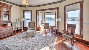 A spacious room with a large wooden floor, a classic chandelier, and a view of a lake through large windows. - 1872 Bethlehem Home w/ View of Ohio River! (Otto)