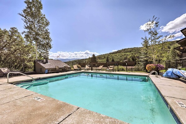 Una piscina rectangular con superficie de agua azul cristalina, rodeada de sillas de descanso y una terraza.