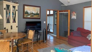 A living room with a dining table, chairs, a TV, a red couch, and a painting on the wall. - Lakeside Escape Steps to Lake Michigan Beach! (Lakeside)