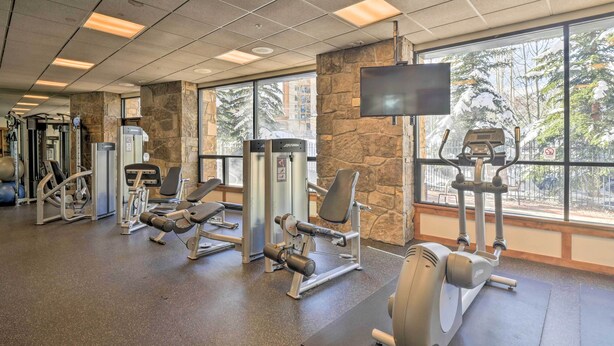 A gym with various exercise equipment, large windows, and a stone wall. - Walk to Lifts: Breck Condo on Main St w/ Amenities (Breckenridge)