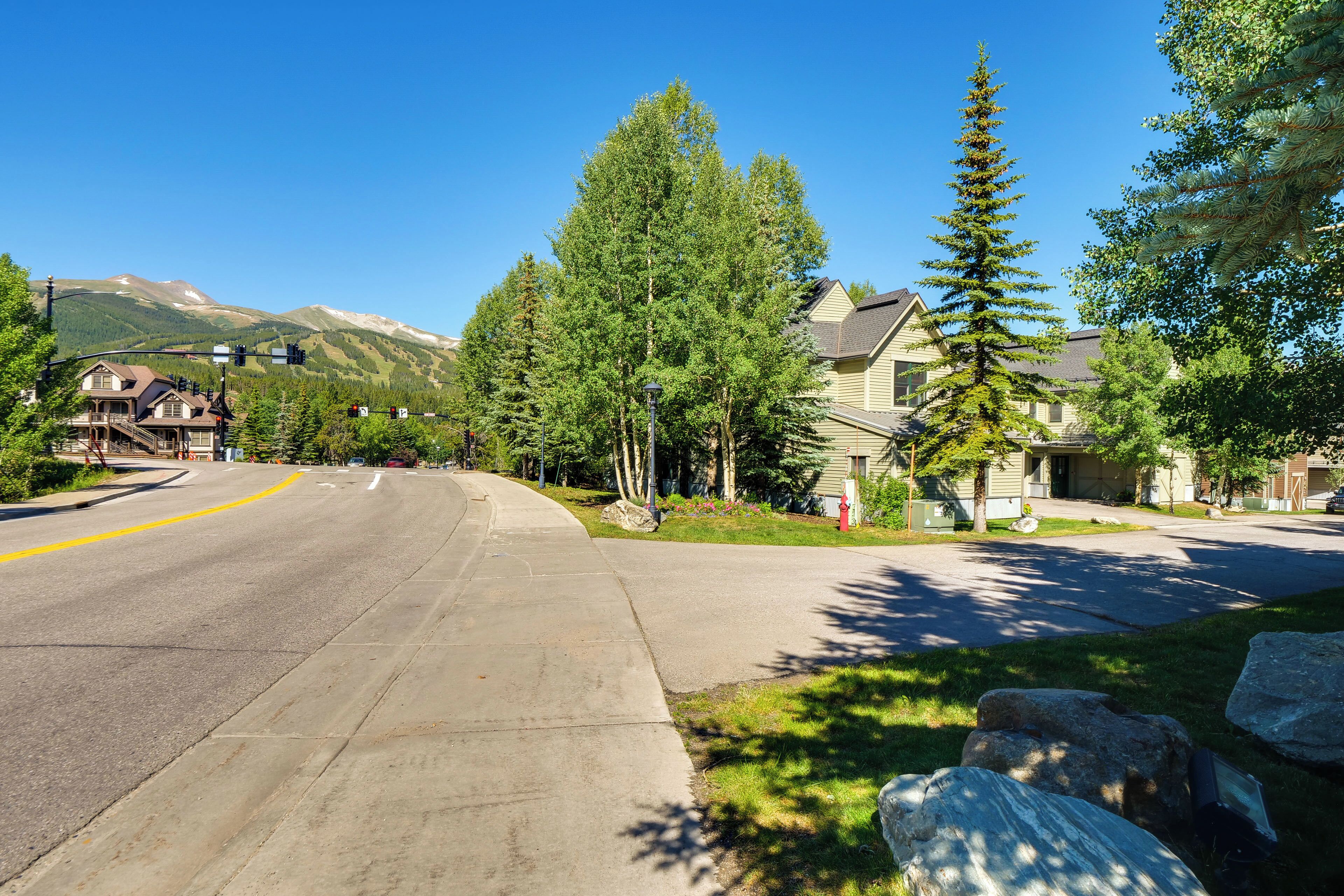 A residential street with houses, a clear sky, and mountains in the background.
