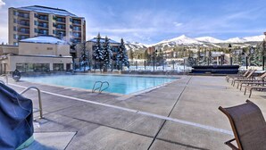 A hotel pool area with a view of snow-capped mountains, lounge chairs, and a building with multiple floors. - Walk to Lifts: Breck Condo on Main St w/ Amenities (Breckenridge)