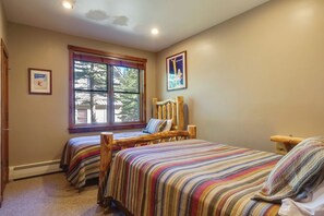 Un dormitorio con dos camas de madera, una ventana con vistas a árboles y un cuadro en la pared.