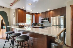 Une cuisine moderne dotée d’un îlot central, de tabourets de bar, d’appareils électroménagers en acier inoxydable et de meubles de rangement en bois.