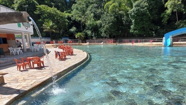 A swimming pool with clear water, surrounded by stone steps and red plastic chairs.
