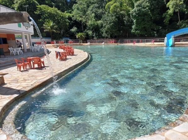 Une piscine à l’eau claire, entourée d’escaliers en pierre et de chaises en plastique rouge.