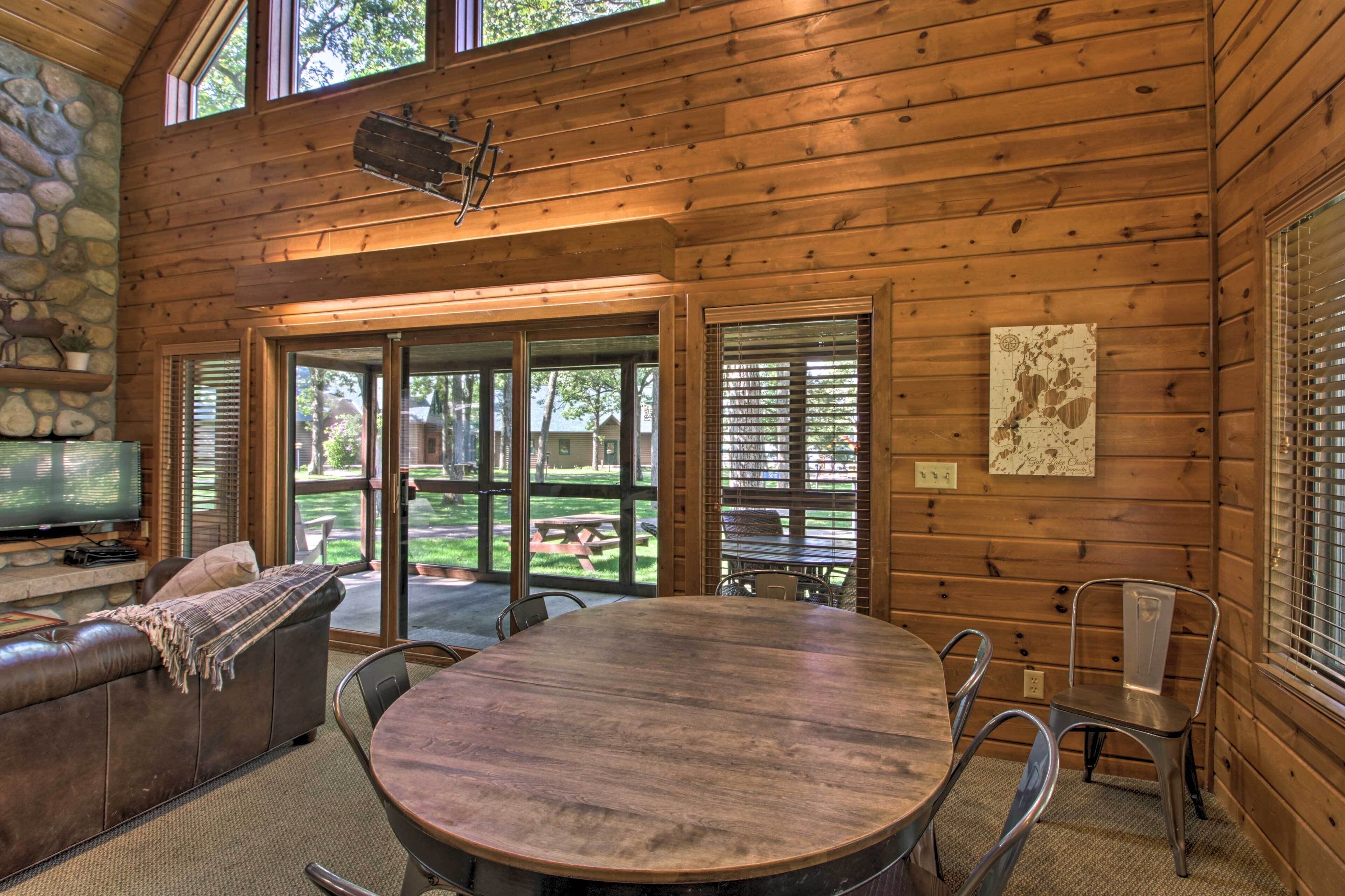 A wooden interior with a round table, chairs, a sofa, and a television.