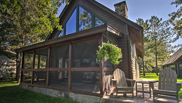 Eine Blockhütte mit großen Fenstern, einem Steinkamin und einer Terrasse mit Adirondack-Stühlen.