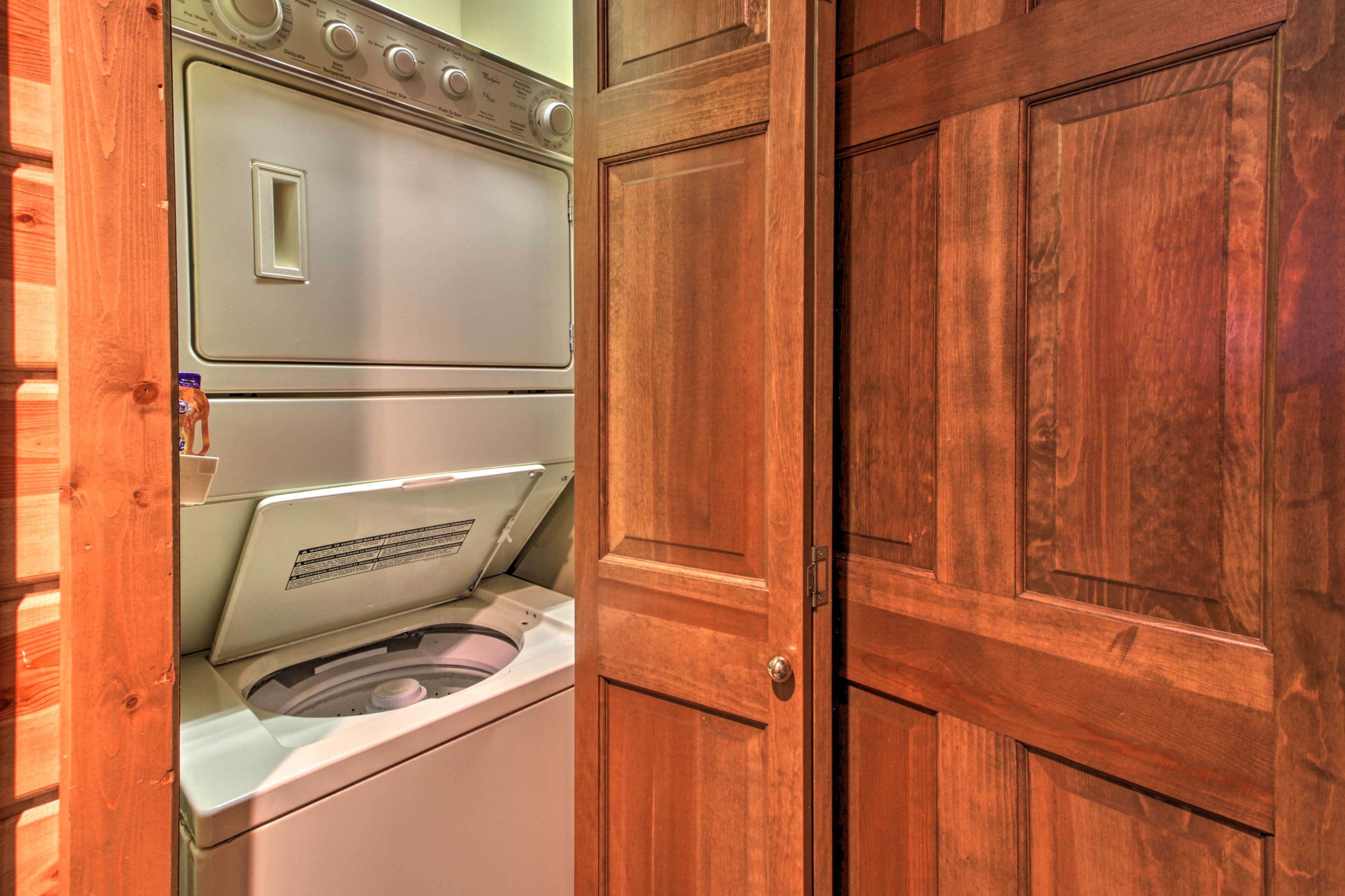 A laundry room with a front-loading washing machine and a dryer, wooden doors, and a wooden wall.