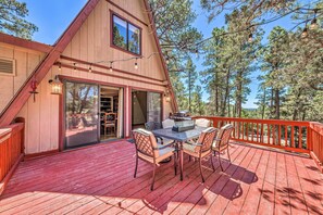 A wooden deck with a dining table and chairs, a red railing, and a view of trees. - Pet-friendly Ruidoso Cabin w/ Deck & Grill! (Ruidoso)