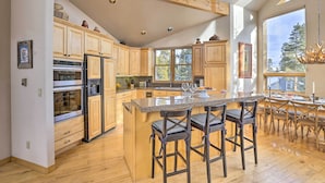 A spacious kitchen with wooden cabinets, a large island with bar stools, and a view of the outdoors through large windows.