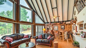 A spacious living area with leather sofas, a round coffee table, and a wooden dining table. Large windows offer views of the outdoors. - A-frame Ruidoso Retreat w/ Deck, Grill & Views! (Ruidoso)