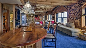 A wooden dining table with chairs, a stone wall, and a sofa in a rustic interior. - Sugar Mountain Resort Condo w/ Pool Table & Views! (Banner Elk)