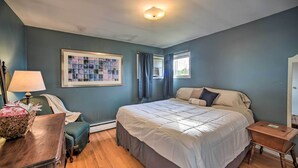 Ein Schlafzimmer mit einem großen Bett, einem Schreibtisch mit Lampe, einem gerahmten Bild an der Wand und einem Fenster mit Vorhängen.