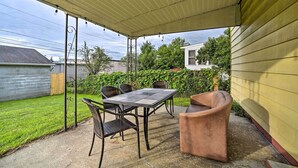 Eine überdachte Terrasse mit Tisch und Stühlen, einer gepolsterten Sitzecke und Blick auf den Garten.