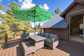 A wooden deck with wicker furniture and a green umbrella. - Spacious & Quiet Pagosa Springs Cabin w/ Deck! (Pagosa Springs)