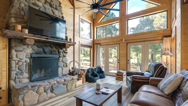 Un interior de cabaña acogedor con chimenea de piedra, sofá de cuero y ventanas amplias.