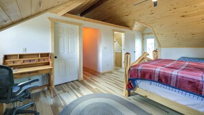 Un dormitorio con techo de madera, una cama con manta escocesa, un escritorio con silla y una escalera de madera.