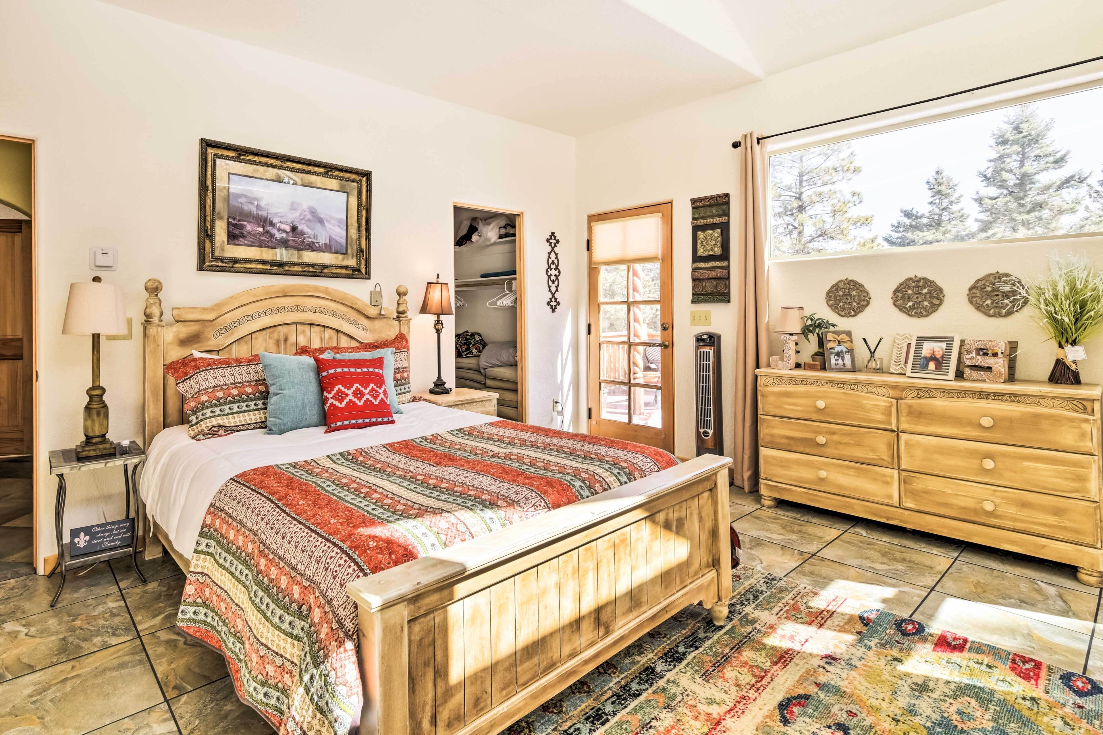 A bedroom with a wooden bed, a dresser, a nightstand, a lamp, a window, and a door.