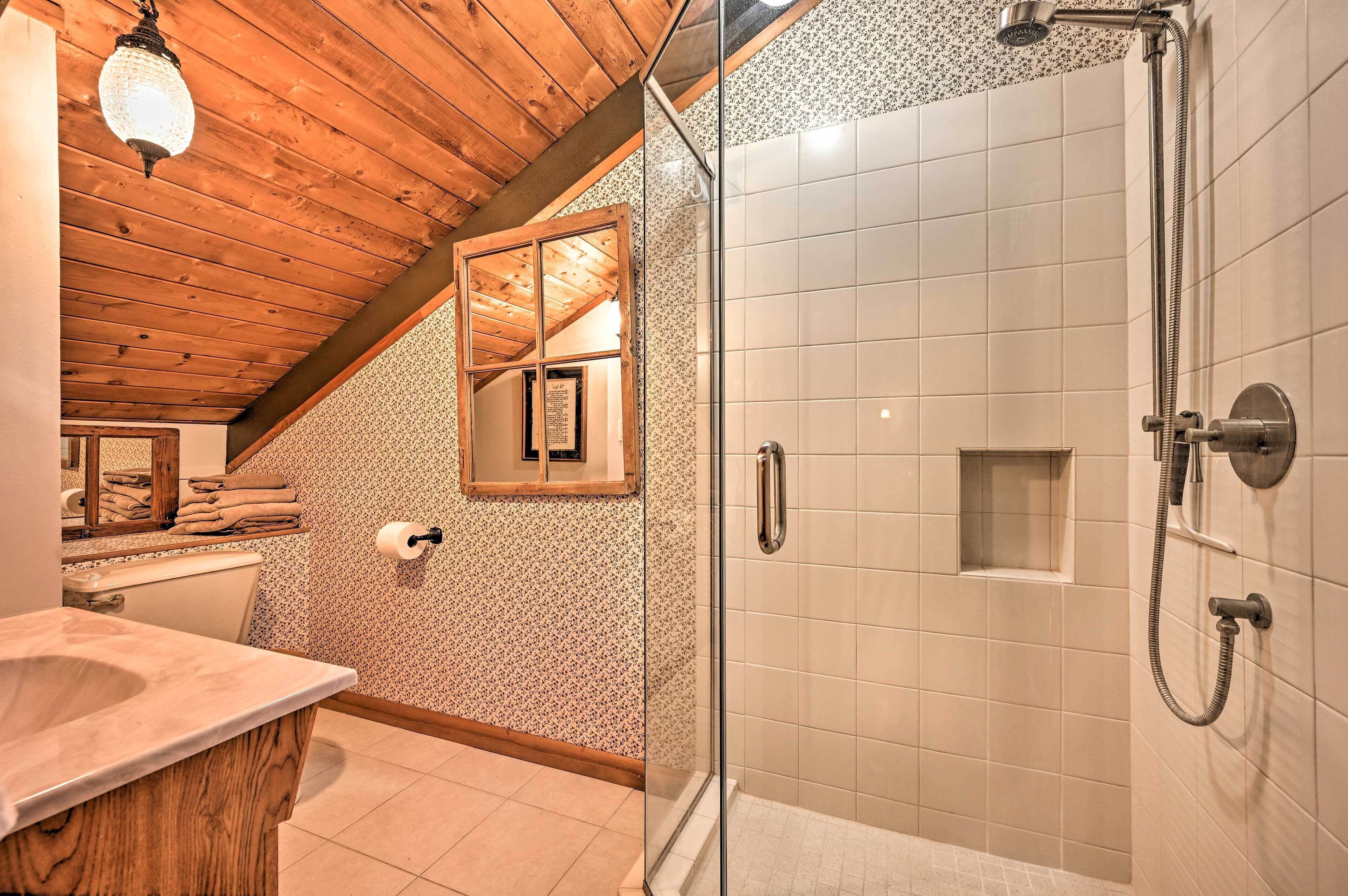 A bathroom with a wooden ceiling, a glass shower enclosure, a marble sink, and a patterned wall.