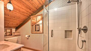 A bathroom with a wooden ceiling, a glass shower enclosure, a marble sink, and a patterned wall.