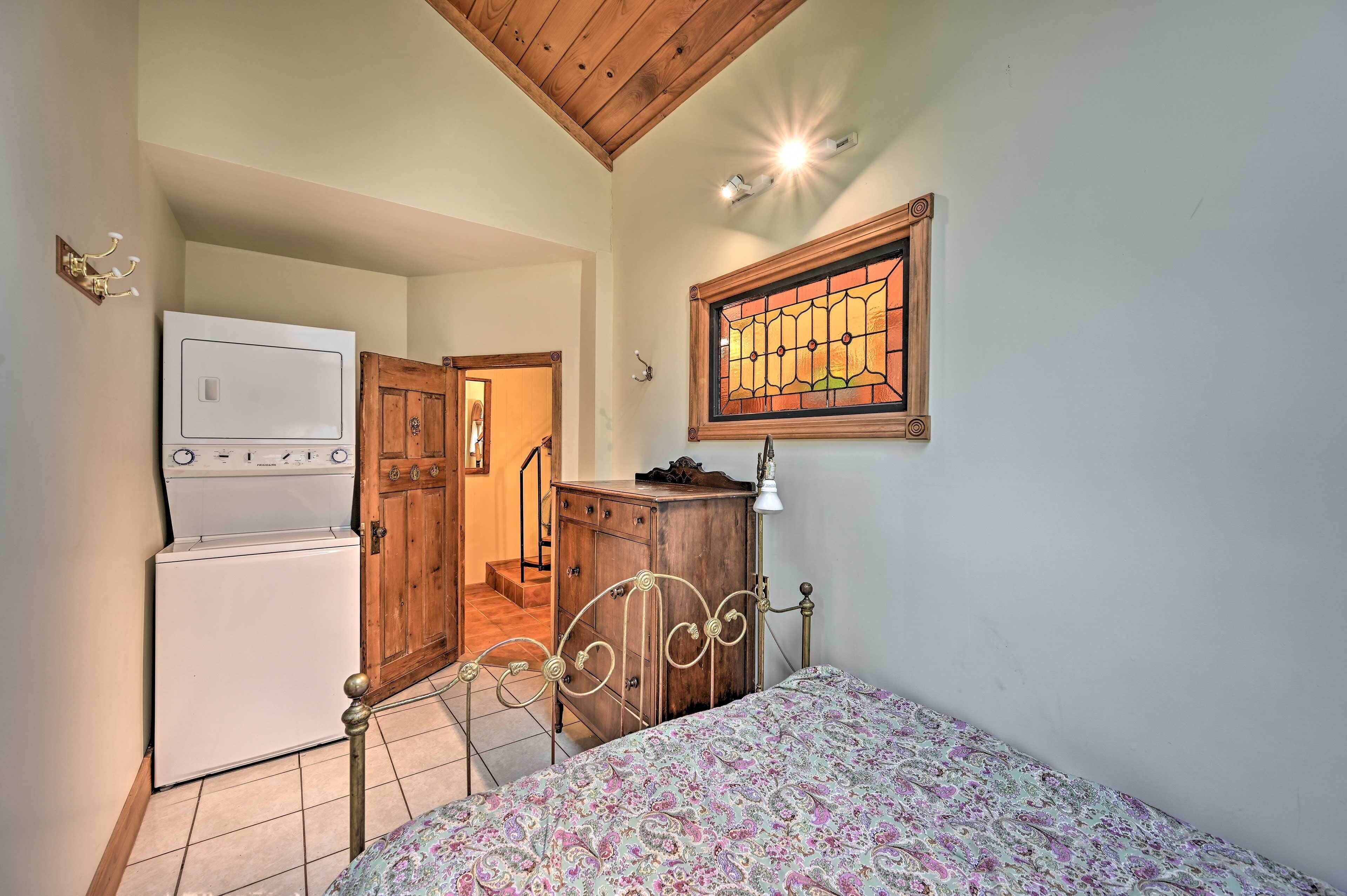 Une chambre à coucher comprenant un lit, une commode, un lave-linge et une porte en bois donnant sur une autre pièce.