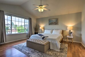 A bedroom with a large window, a ceiling fan, a bed with white bedding, a bedside table with a lamp, and a small nightstand with a fan. - Spacious Thornton Home: 15 Mi to Downtown Denver! (Thornton)