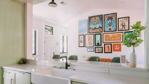 A kitchen with a white countertop, green cabinets, and a sink. There are framed artworks on the wall above the counter. - Sacramento Guest House w/ Patio ~ 5 Mi to Downtown (Sacramento)