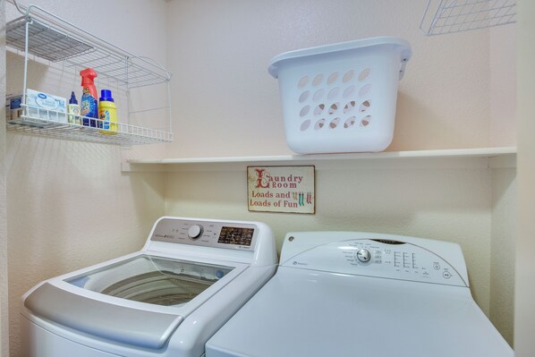 A laundry room with two washing machines, a shelf with cleaning supplies, and a basket.