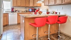 A modern kitchen with wooden cabinets, a built-in microwave, a coffee maker, and a red fruit bowl on the island.