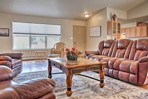 A living room with a brown leather sofa, a wooden coffee table, and a large window. - Montrose Townhome 13 Mi to Black Canyon Natl Park (Montrose)