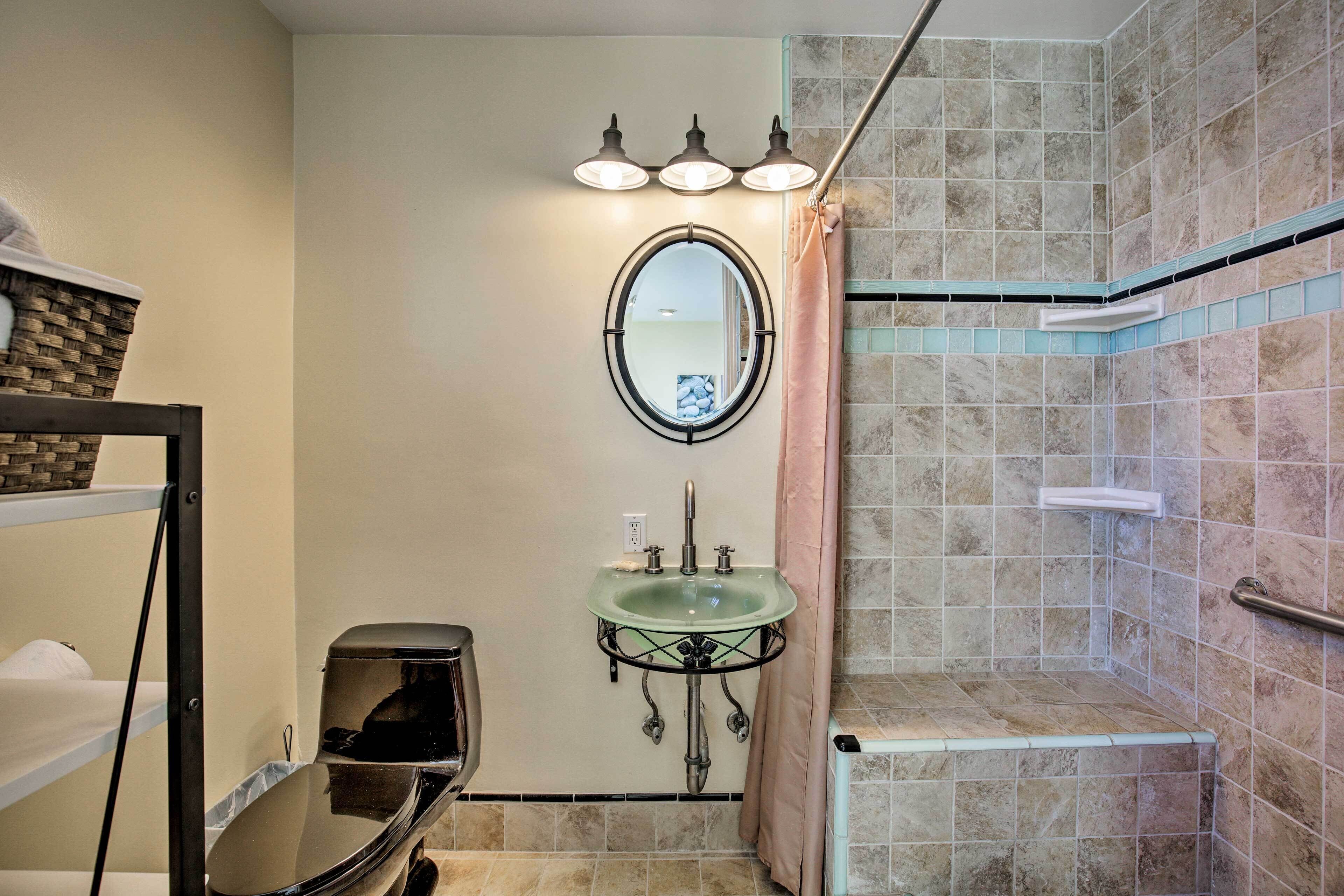 A bathroom with a glass sink, a round mirror, and a shower area with tiled walls.