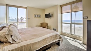 Un dormitorio con una cama grande, una silla, un televisor y vista al mar.