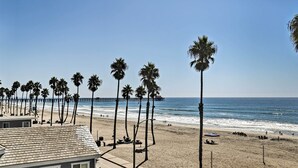 A beach with palm trees, a pier, and a building with a tiled roof. - Beachfront Oceanside Condo w/ Pool & Hot Tub! (Oceanside)