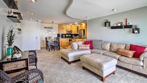 Una sala de estar moderna con un sofá color beige, un comedor con mesa y sillas, y una cocina al fondo.