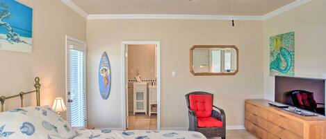 Een slaapkamer met een bed, een stoel, een kaptafel, een televisie en een plafondventilator.