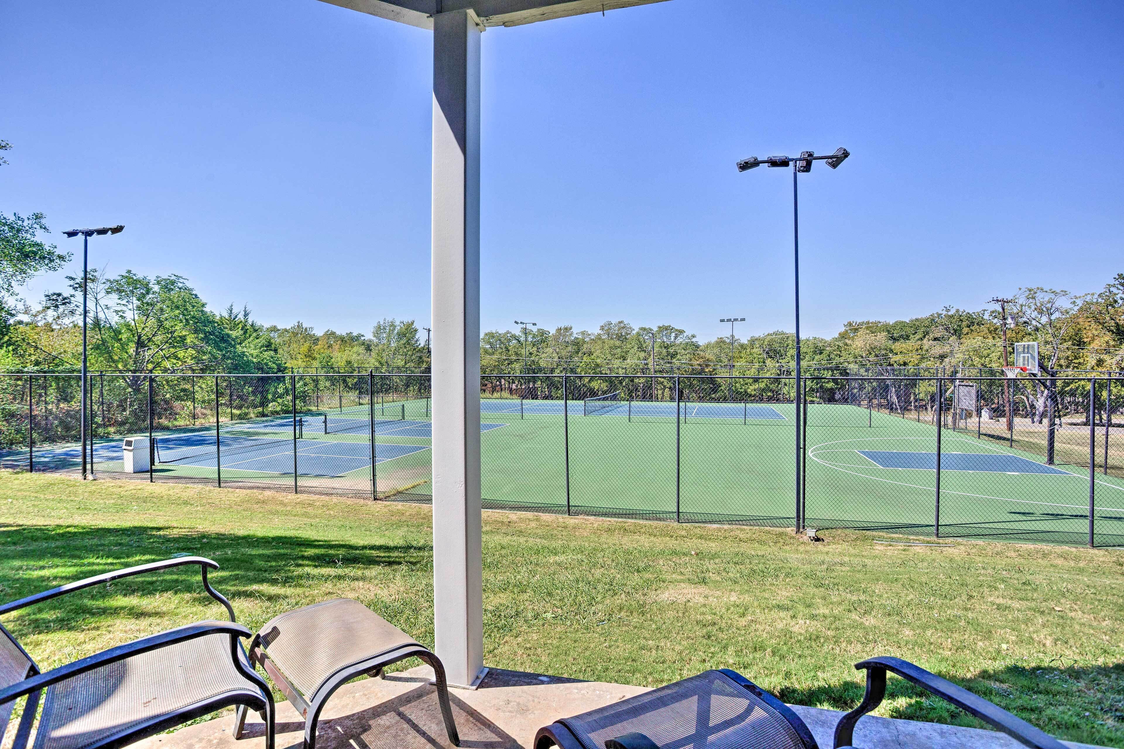 Een tennisbaan met een overdekte zithoek en een hek.