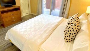 A bedroom with a bed, a TV on a wooden dresser, and a door leading to a balcony. - 3 Bedroom Townhome in Osoyoos with lake views! XI (Osoyoos)