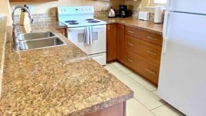 A kitchen with wooden cabinets, a granite countertop, a stove, a sink, and a refrigerator. - 3 Bedroom Townhome in Osoyoos with lake views! XI (Osoyoos)
